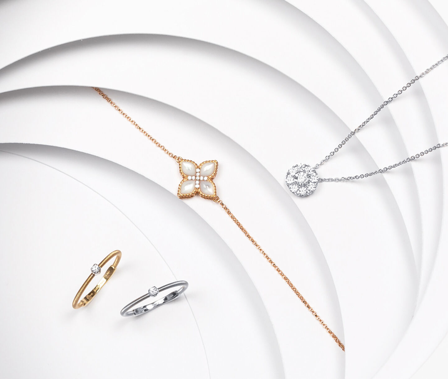 Two gold rings sit beside a necklace with mother of pearl and diamond pendants